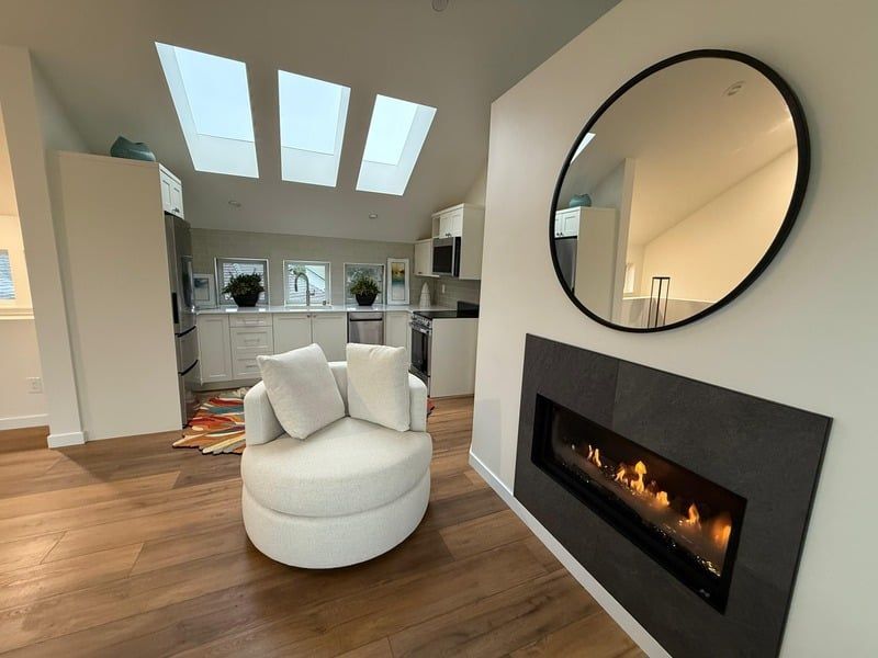 Modern living room with fireplace, round chair, and kitchen in the background. Skylights illuminate the space.