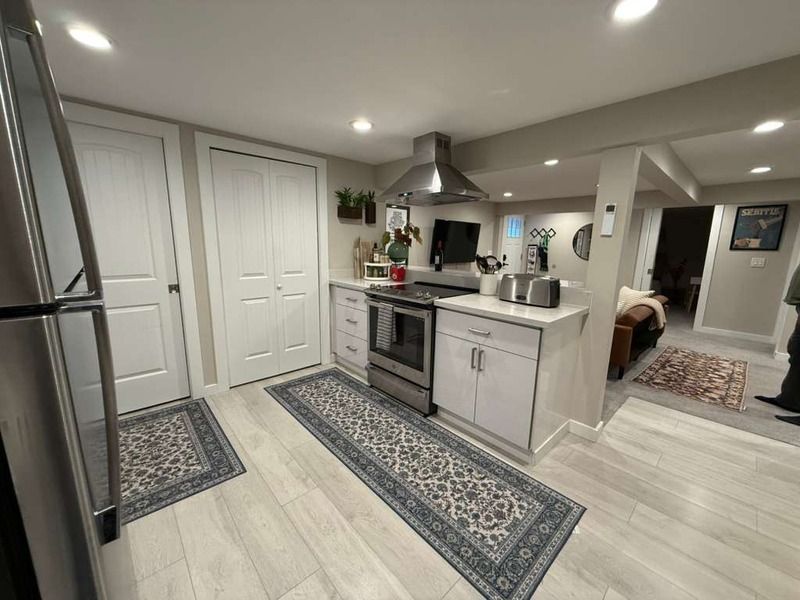 Small kitchen with white cabinets, stainless steel appliances, and patterned rugs on a light wood floor.