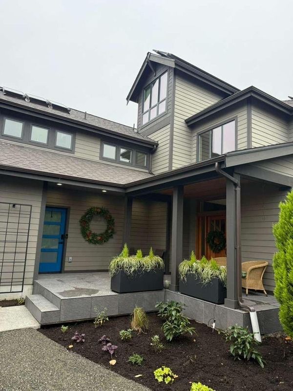 Modern house exterior with gray siding, blue front door, and planters with greenery.