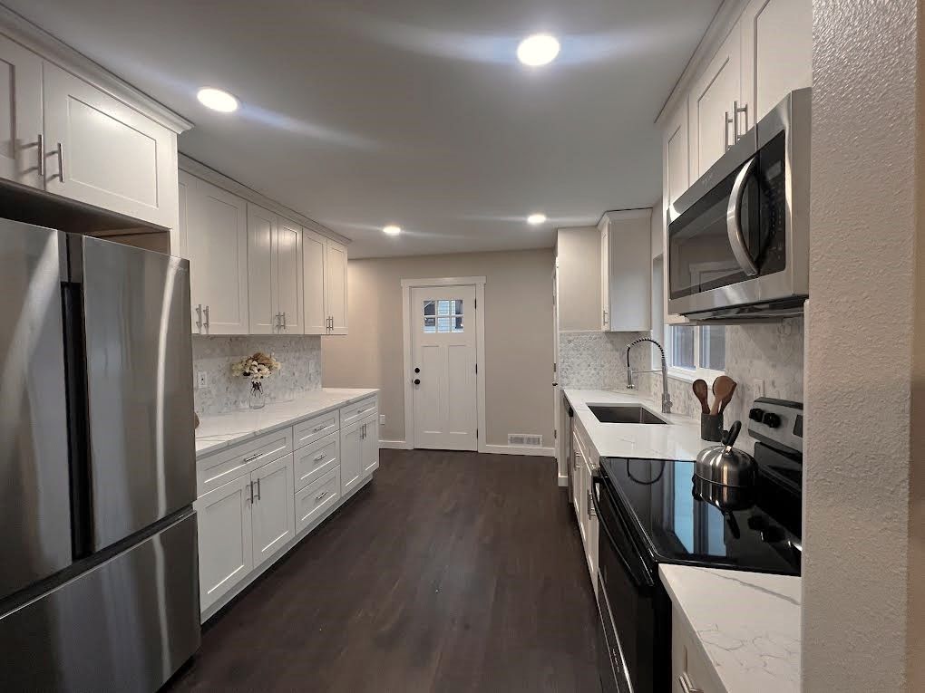 Modern white kitchen with stainless steel appliances, dark wood floors, and bright lighting.