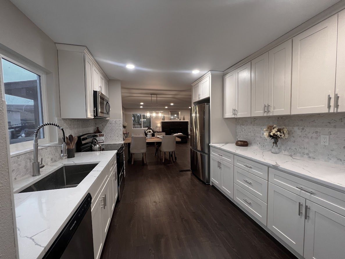 Long kitchen with white cabinets, dark wood floor, and stainless steel appliances.