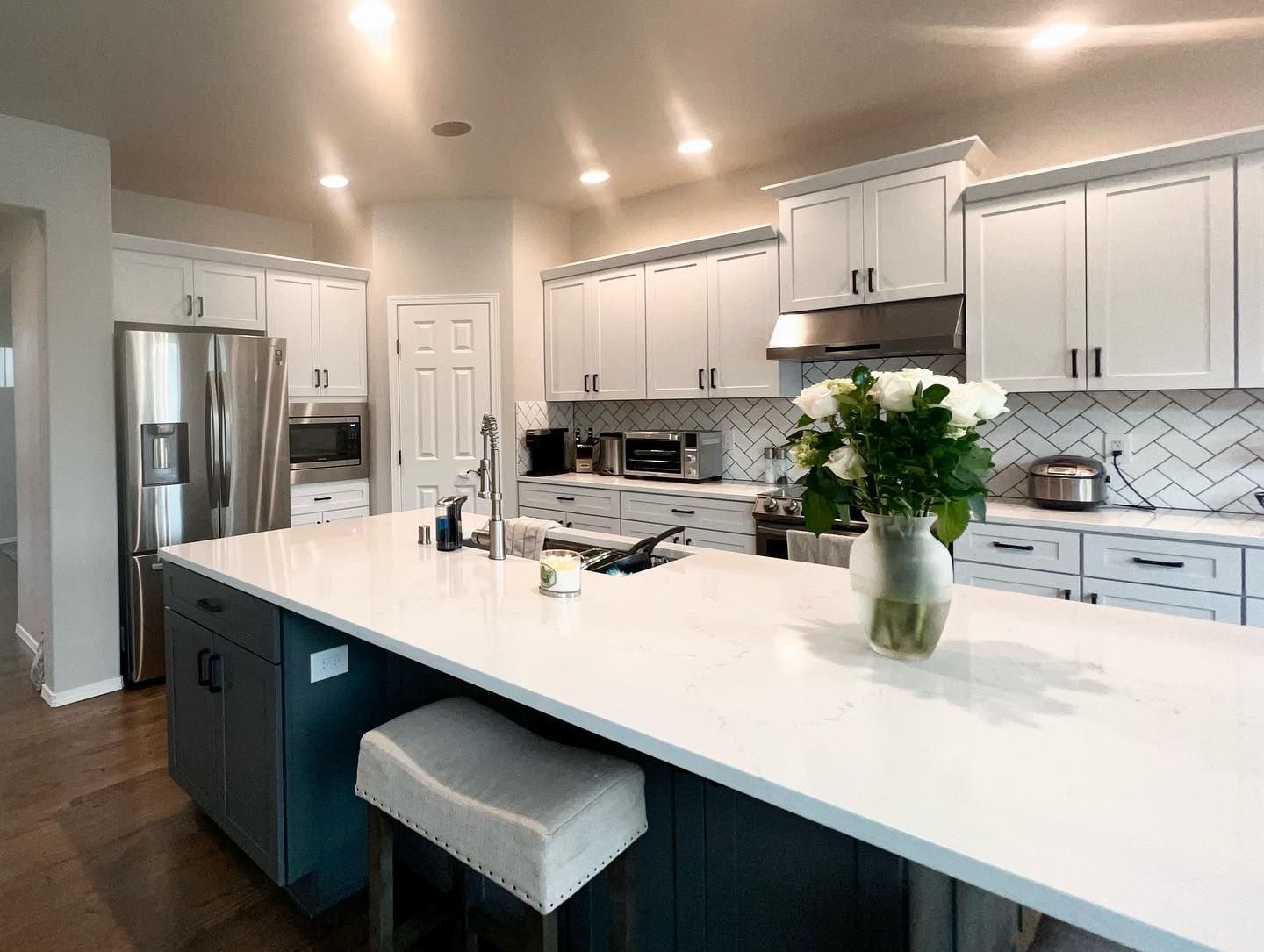 Modern kitchen with white cabinets, dark blue island, stainless steel appliances, and white countertops.