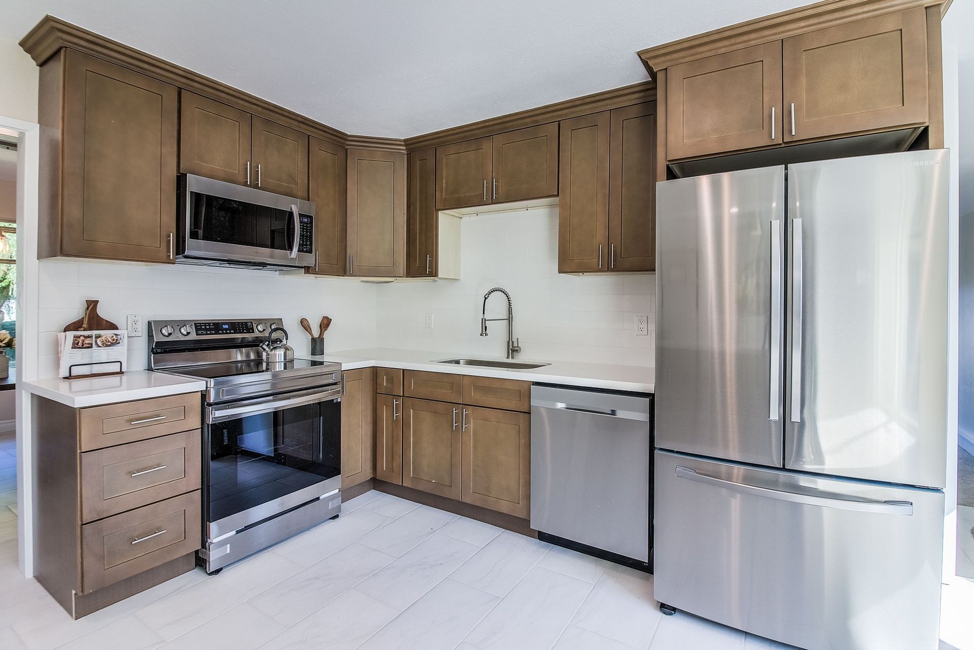 A modern kitchen with brown cabinets, stainless steel appliances, and white countertops.