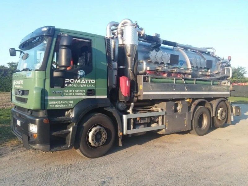 Camion della nettezza urbana verde con serbatoio argentato, parcheggiato all'aperto.