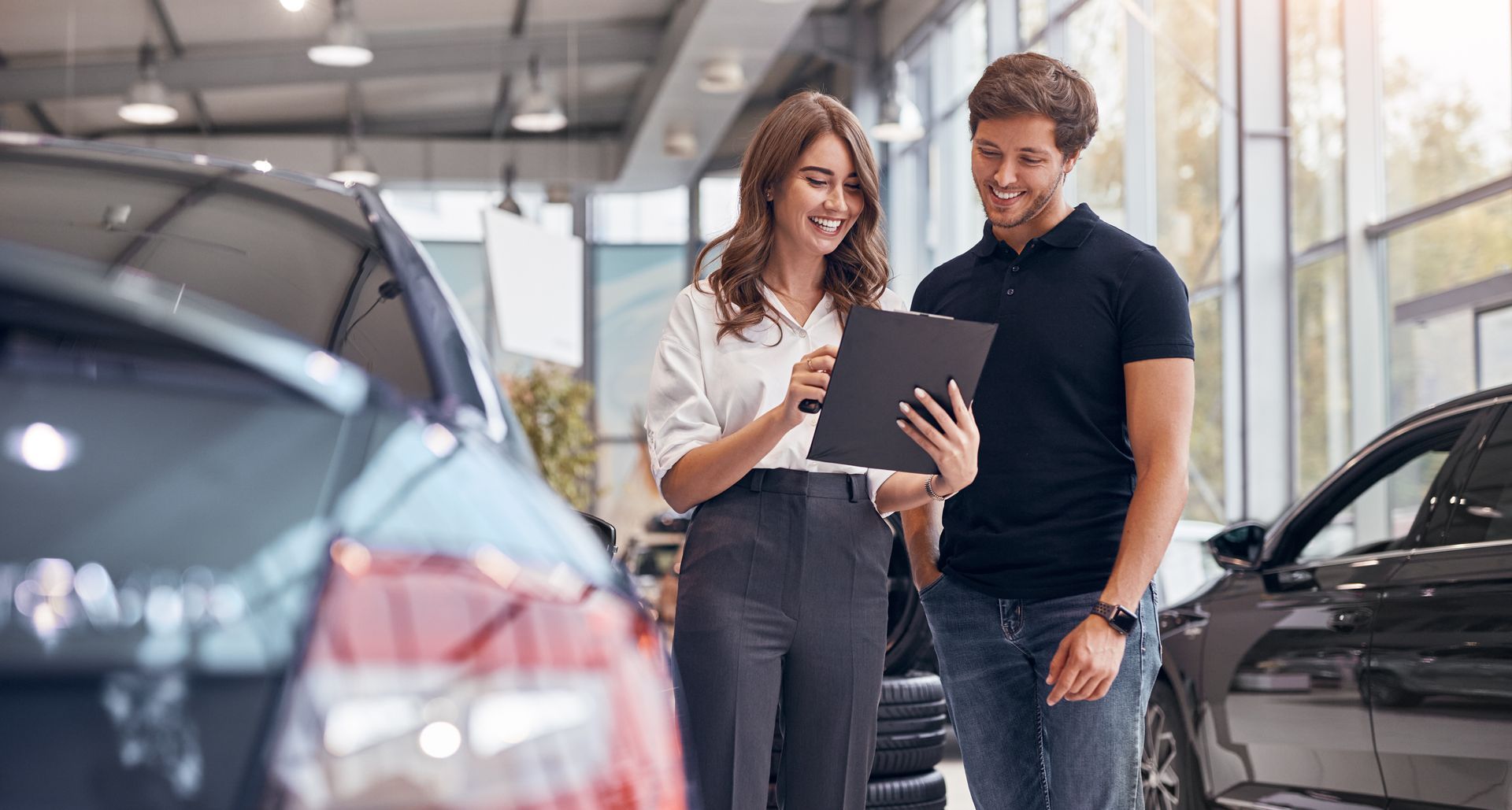 A man and a woman are looking at a clipboard in a car showroom.