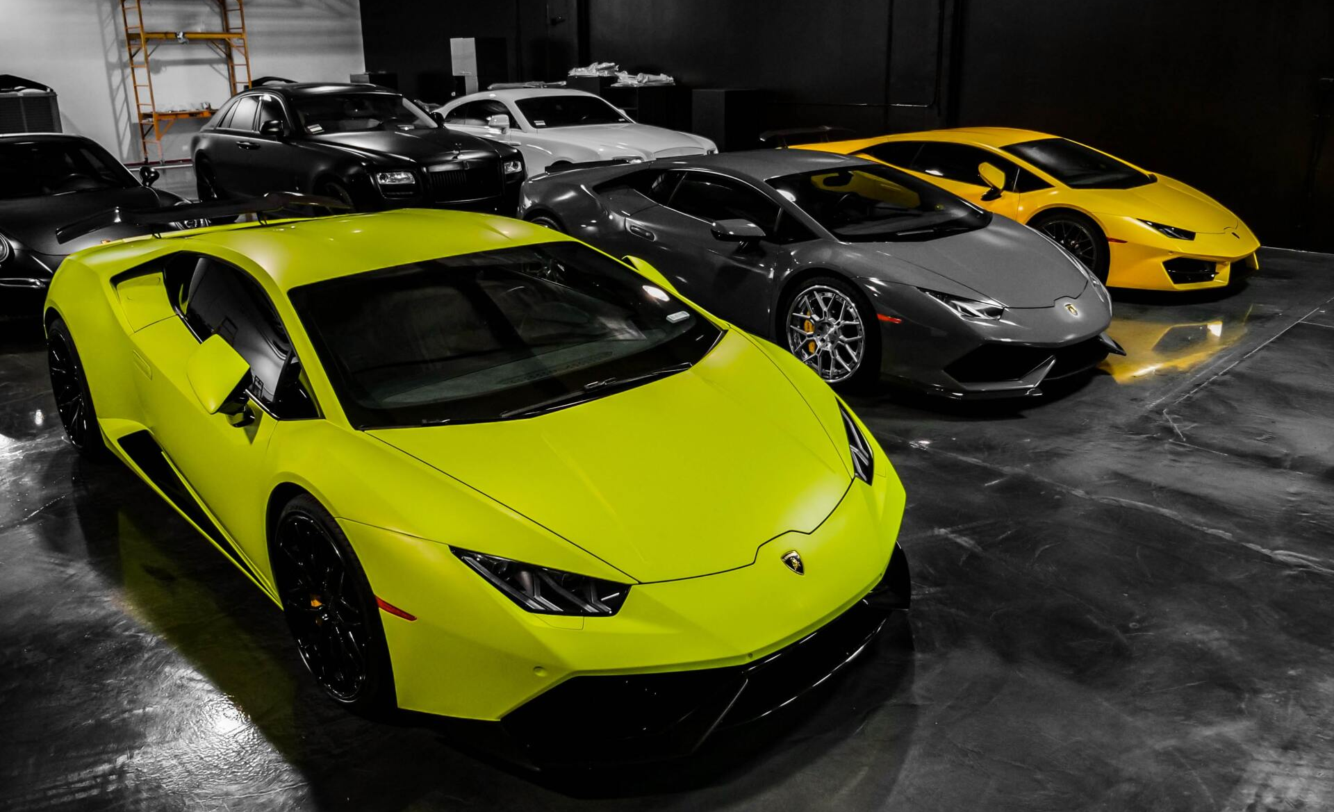 Several luxury cars in a garage, including yellow and gray Lamborghinis.