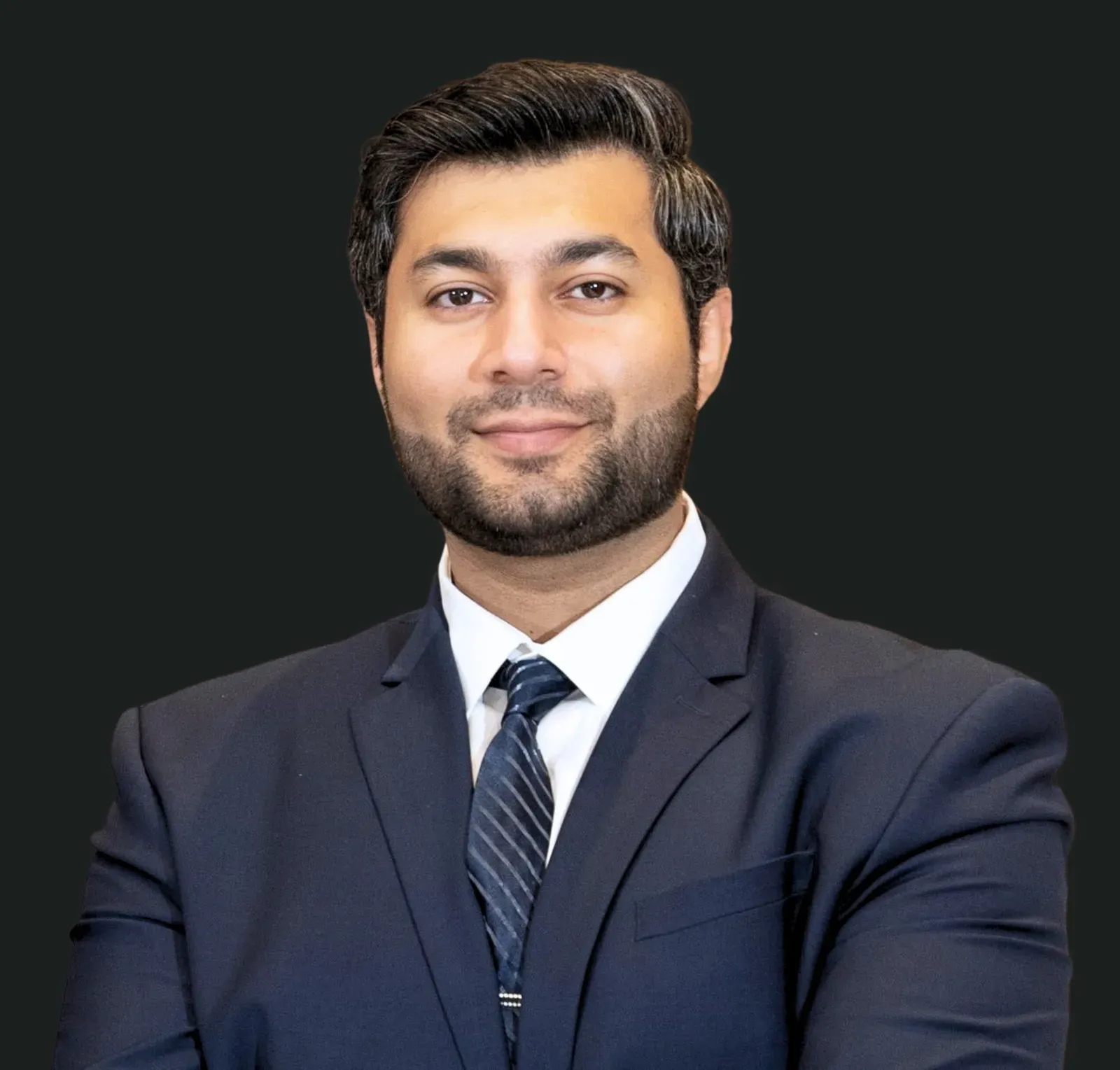 Man in a suit smiles, against a dark background. He has short dark hair and a beard.