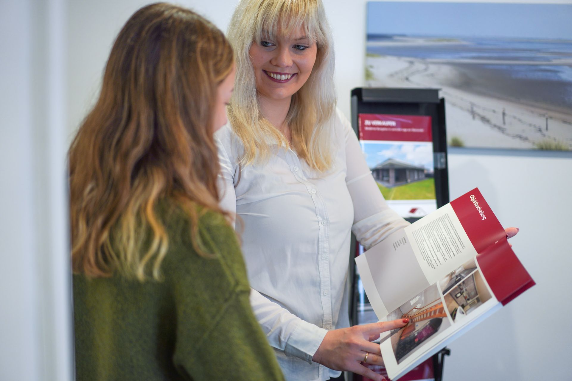 Eine Frau zeigt einer anderen Frau in einem Büro eine Broschüre.