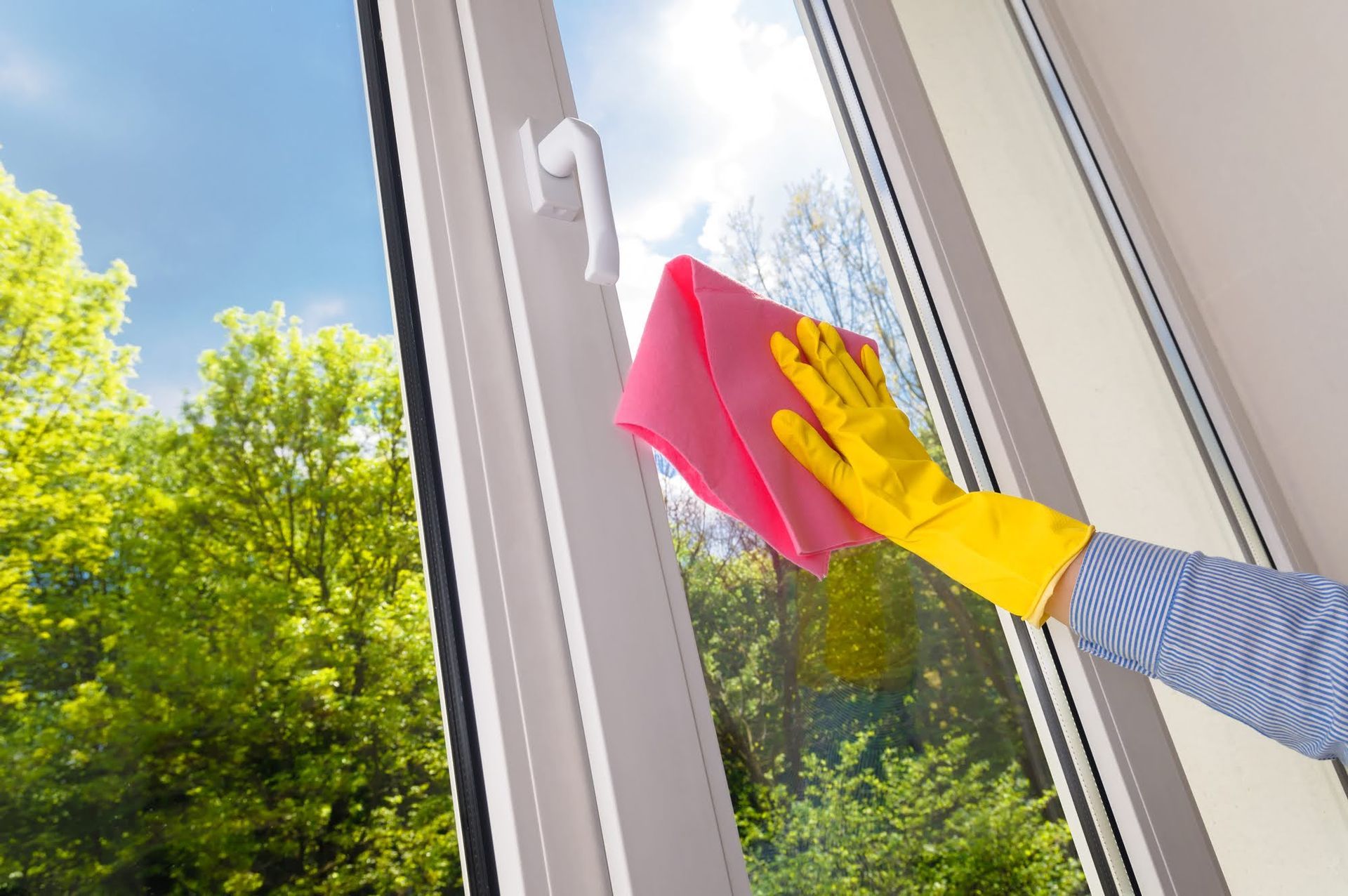 A person wearing yellow gloves is cleaning a window with a pink cloth.