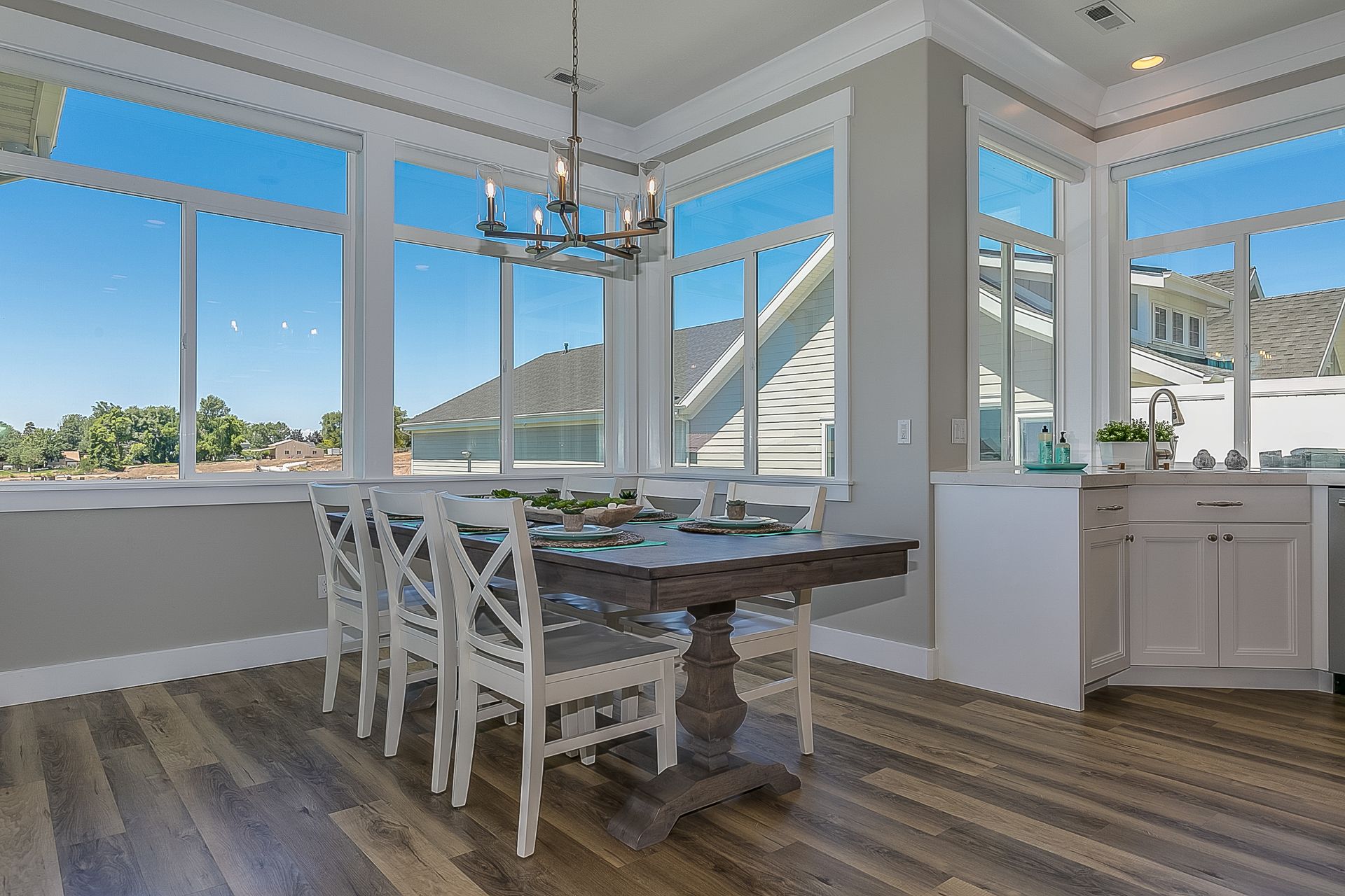 Dining room with table and chairs, large windows, and a chandelier, overlooking a sunny view.