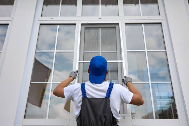 Worker in overalls and a blue cap installing a window frame.