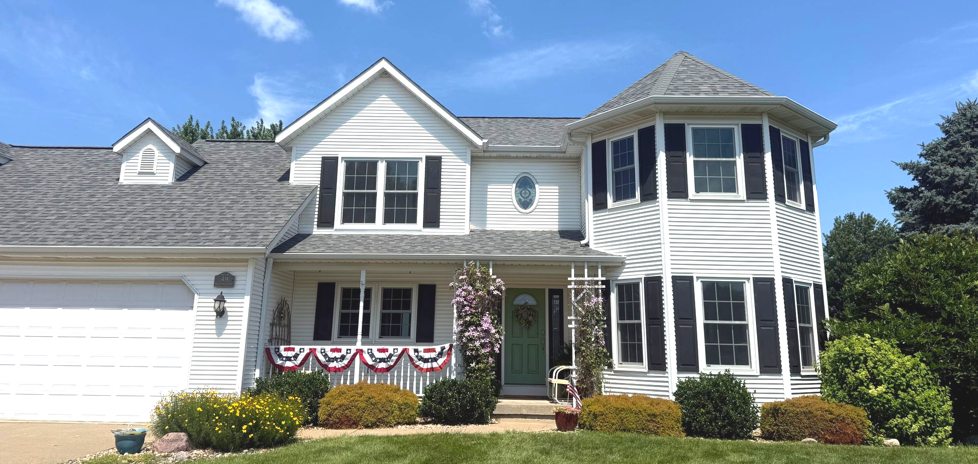 White house with black shutters, green door, and garland. Blue sky.