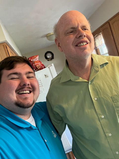 Two smiling men; one in a green shirt, the other in blue, indoors.