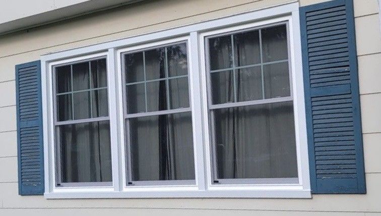 Three-pane window with white trim and blue shutters, on a beige house.