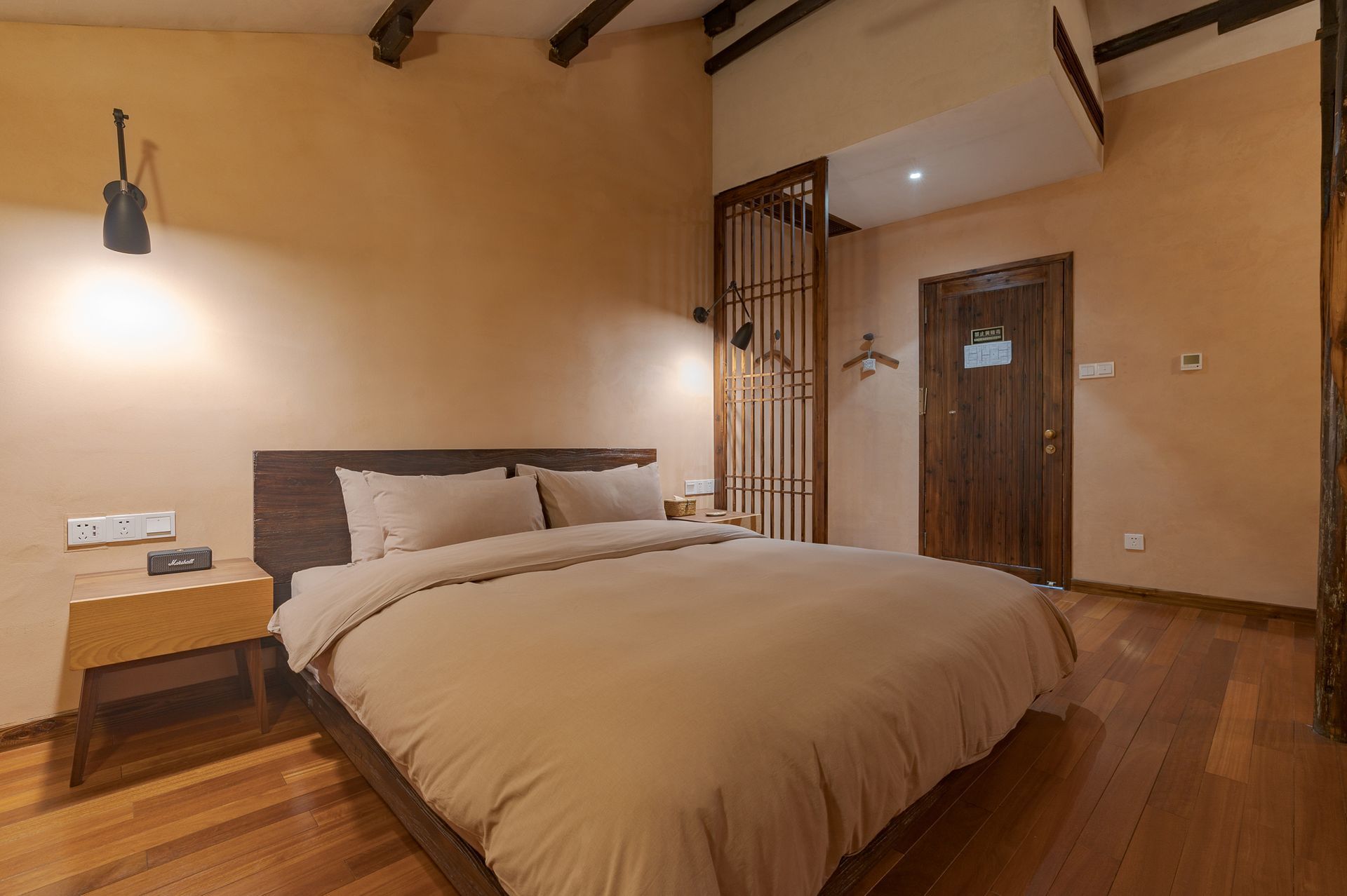 Cozy hotel bedroom with a large bed, wooden floor, and warm beige walls