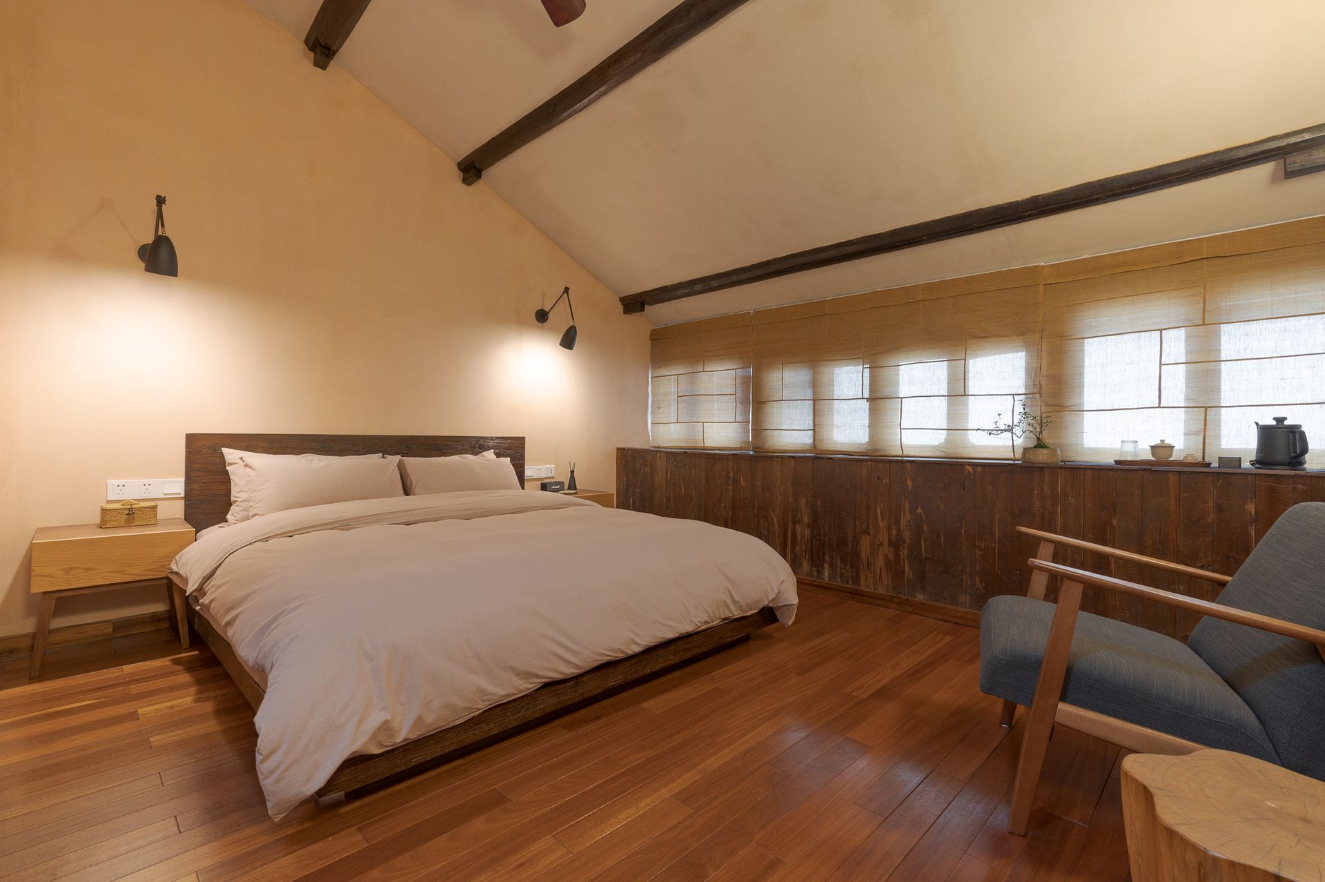 Bright bedroom with a large bed, wood floors, exposed beams, and windows along the wall.