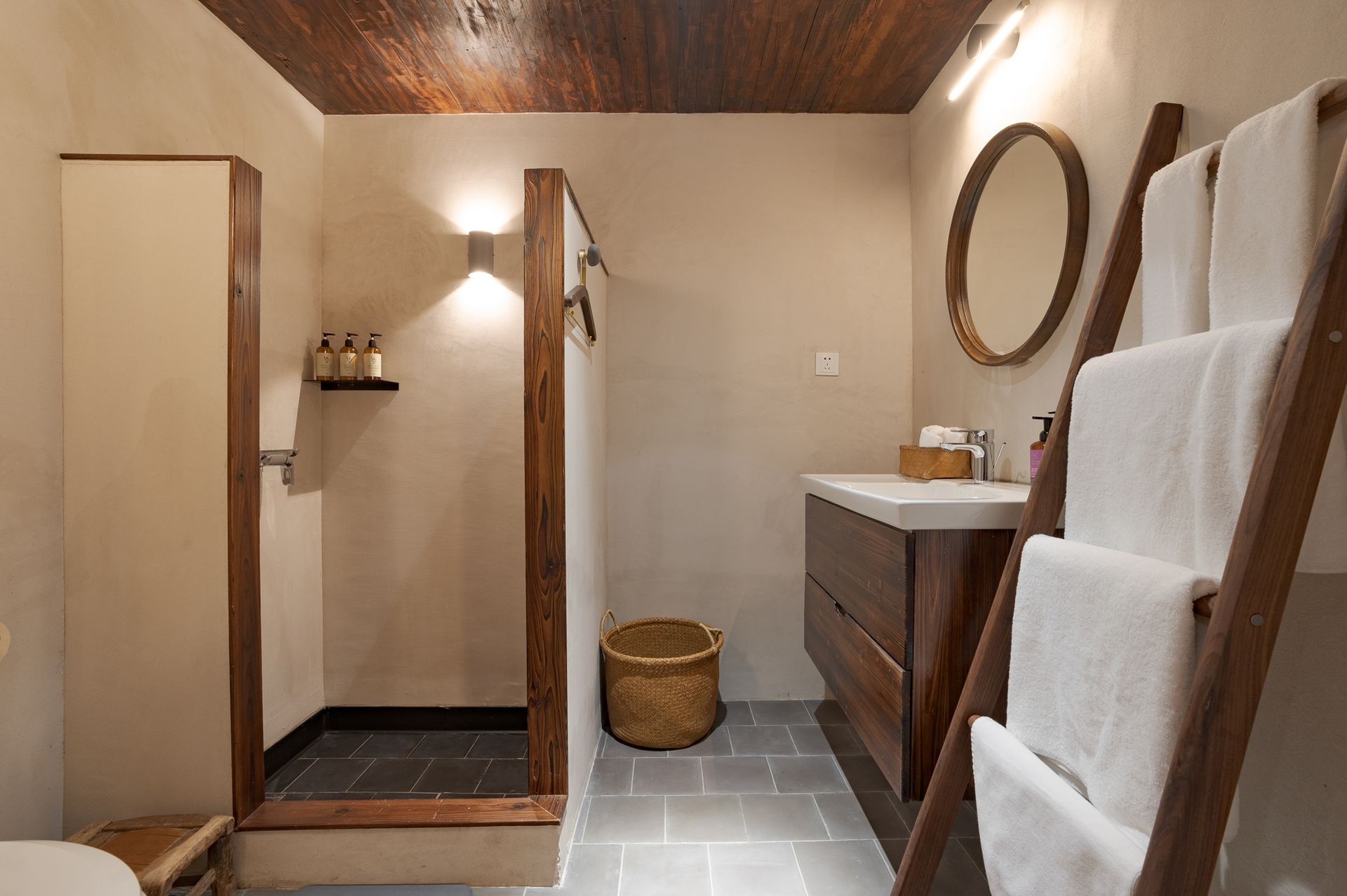 Modern bathroom with wood vanity, open shower, woven basket, and stacked white towels