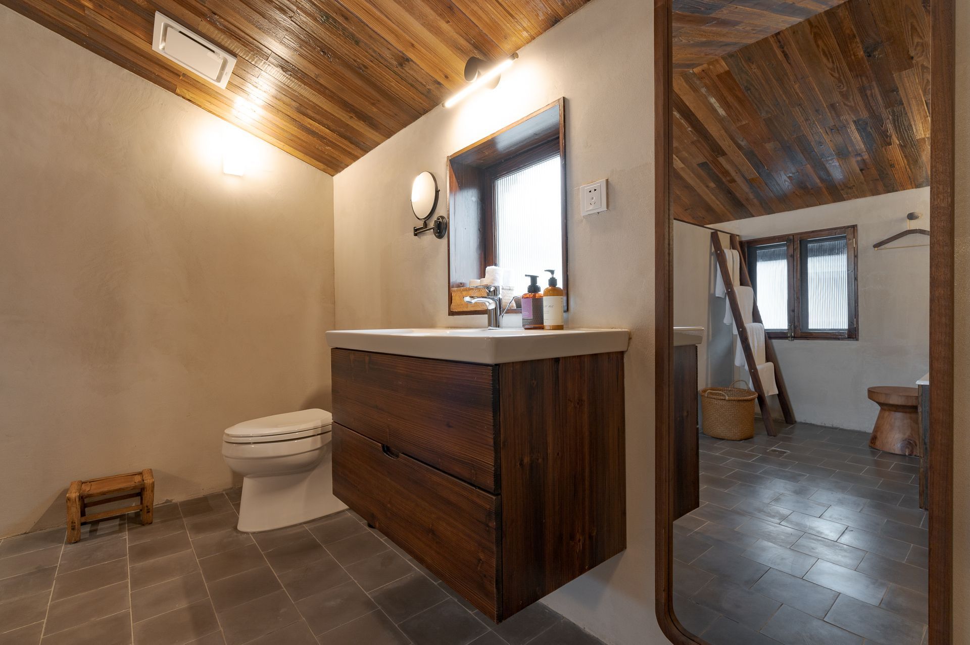 Rustic bathroom with wood ceiling, dark vanity, toilet, and tiled floor, viewed through an open doorway
