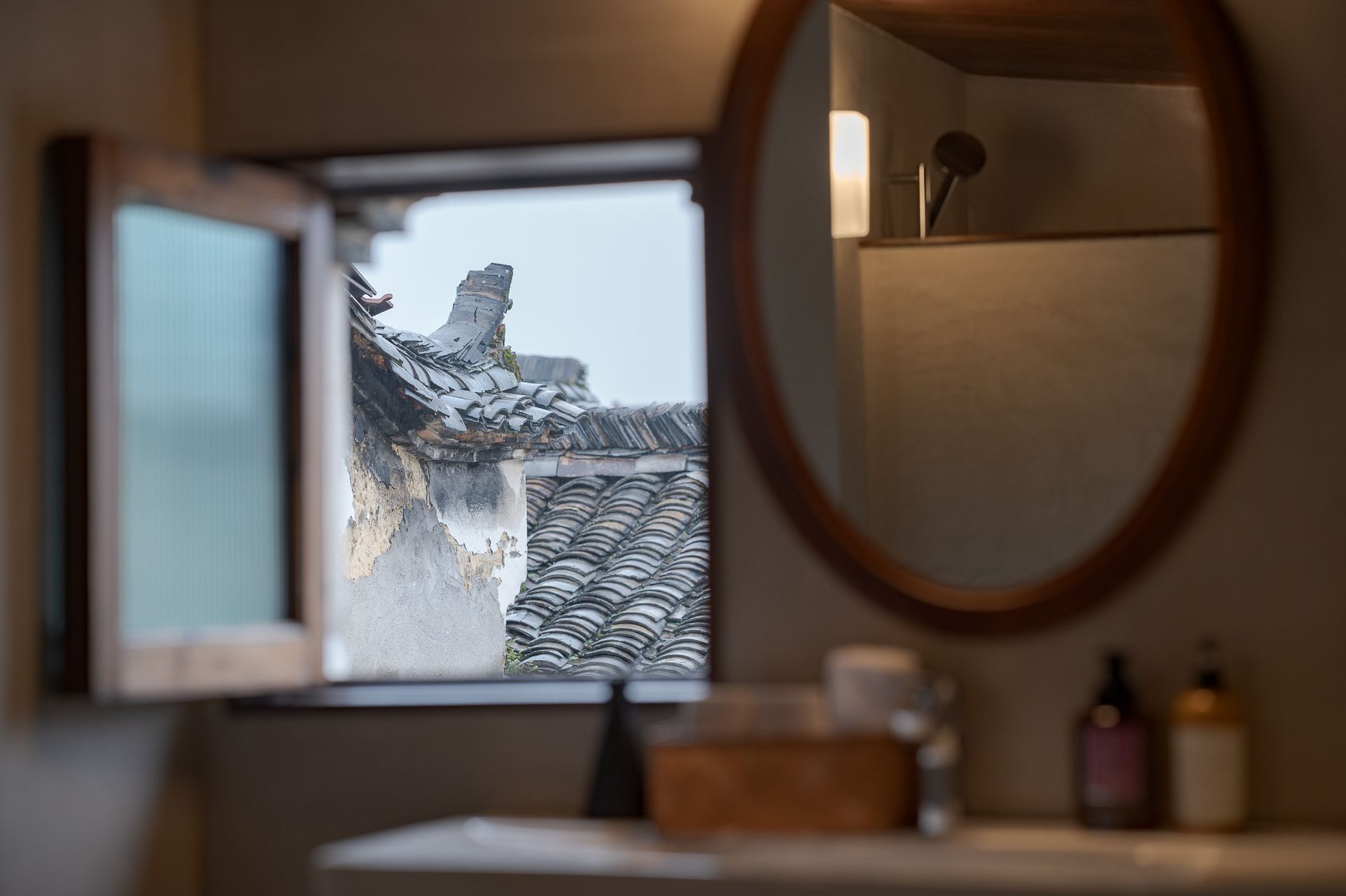 Bathroom mirror reflecting a snowy rooftop outside a small open window
