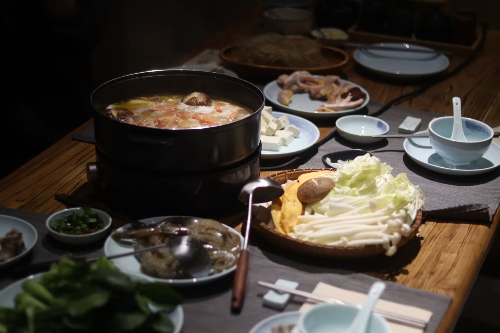 韓式火鍋擺放在木桌上，配有湯底、蔬菜、小菜和餐具。