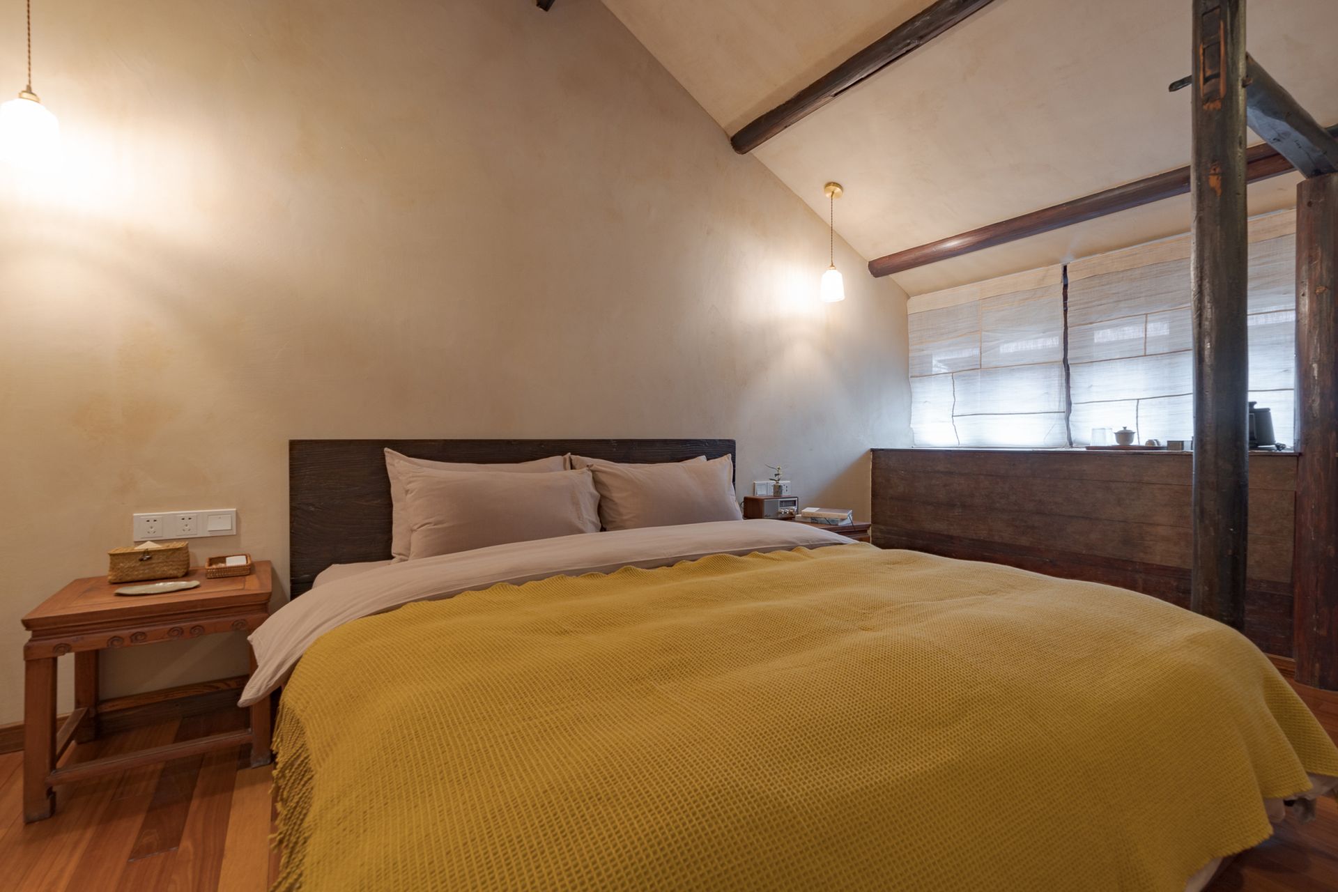 Cozy bedroom with a wooden bed, mustard blanket, nightstand, and sloped ceiling with exposed beams
