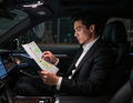 Man in a black suit reading a map inside a car at night