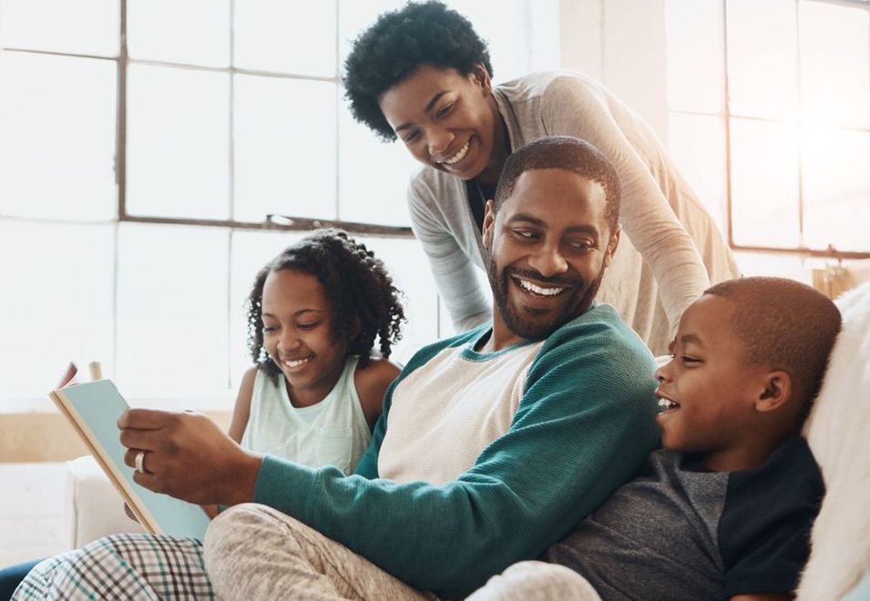 A family is sitting on a couch reading a book together.