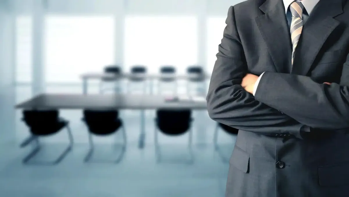 Uomo in giacca e cravatta con le braccia incrociate in una sala conferenze.