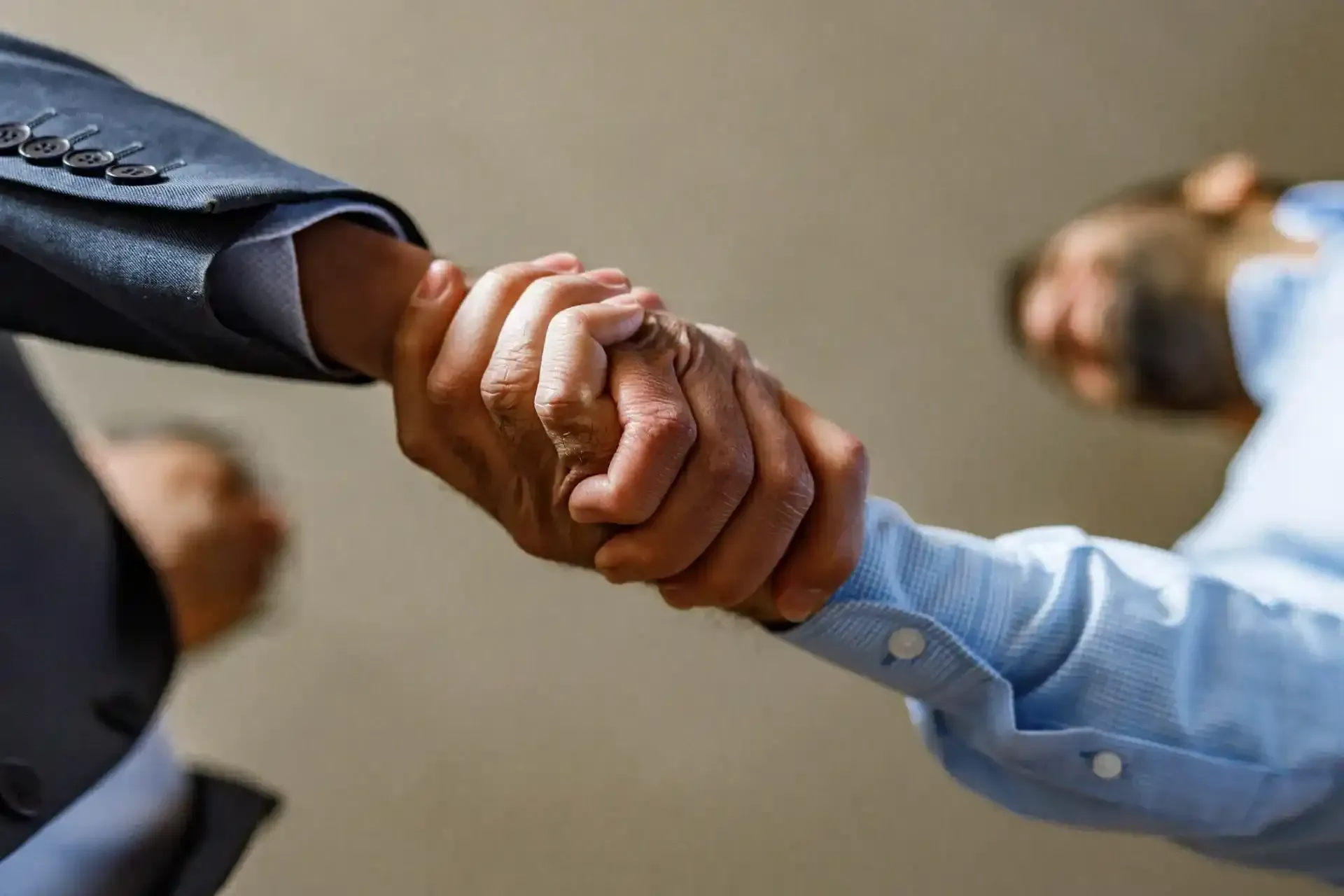 Due uomini in abiti da lavoro si stringono la mano, primo piano, in un interno.