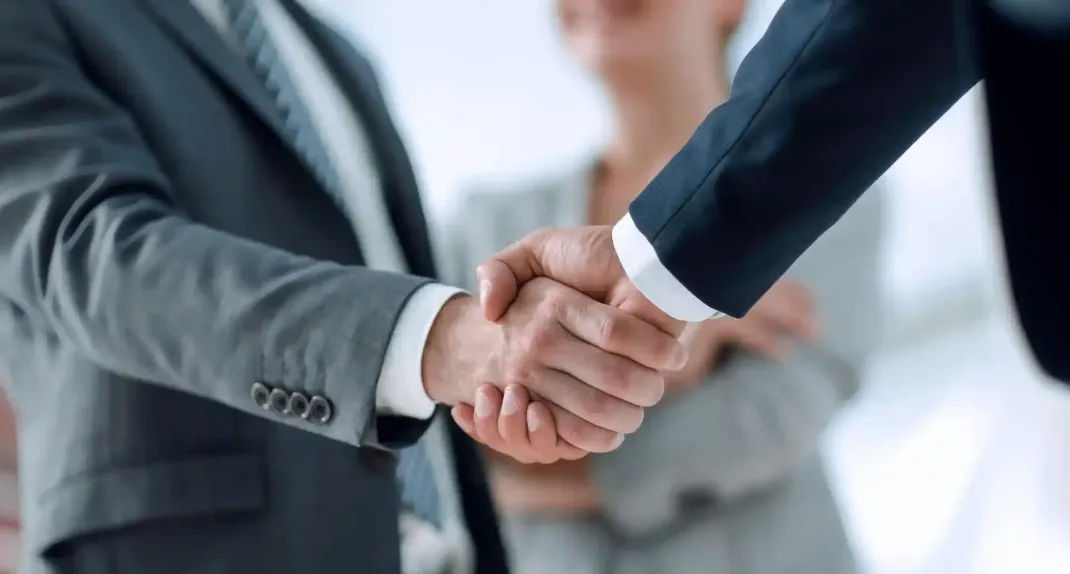 Una donna conduce una presentazione in un ufficio; le persone sono sedute attorno a un tavolo, un computer portatile e una lavagna.