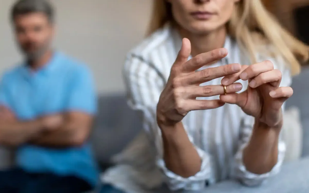 Donna che si toglie la fede nuziale; sullo sfondo un uomo con le braccia incrociate, il che suggerisce problemi relazionali.