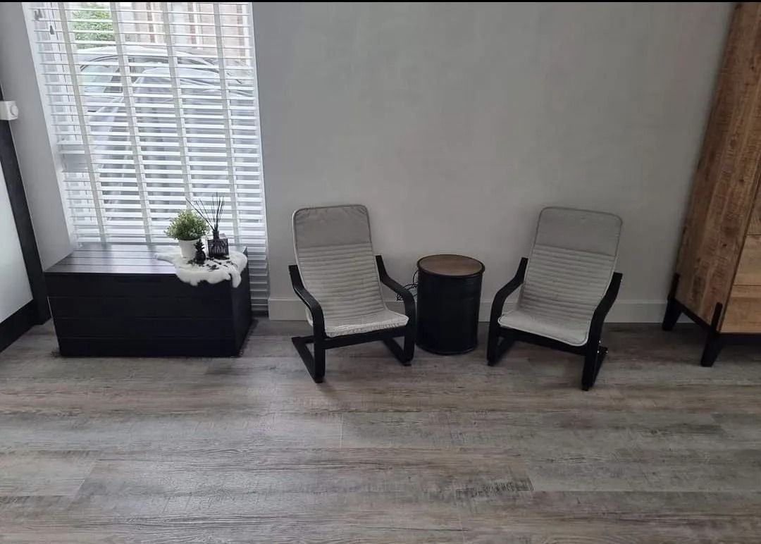 Een kleine hoek met kunstgras, een houten schutting, grijze bestrating en blauwe tuinspullen achterin.