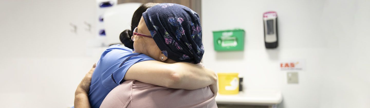 A person wearing a patterned head covering hugs a medical professional in a clinical setting.