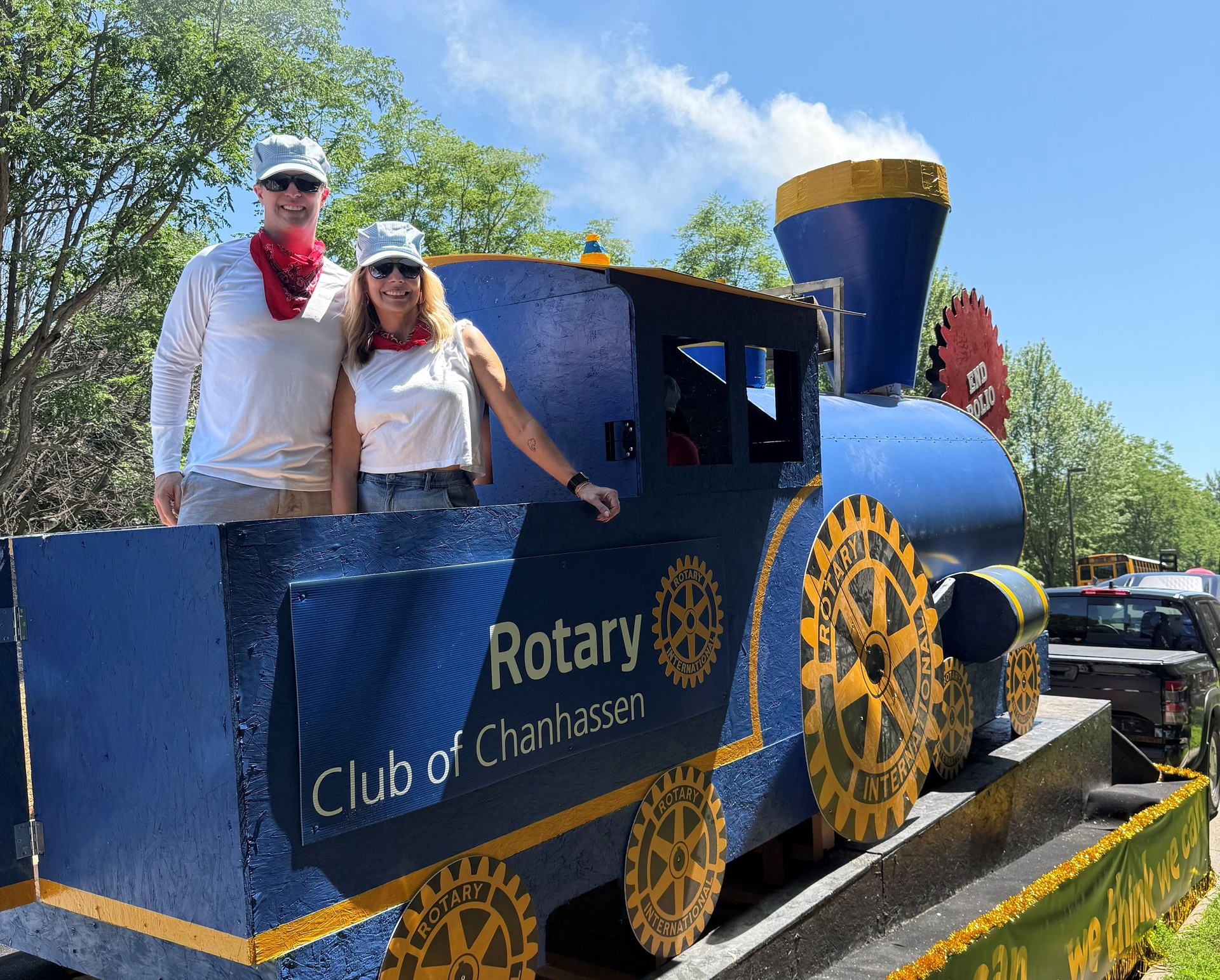 Two people pose on a blue Rotary Club train float in a parade.