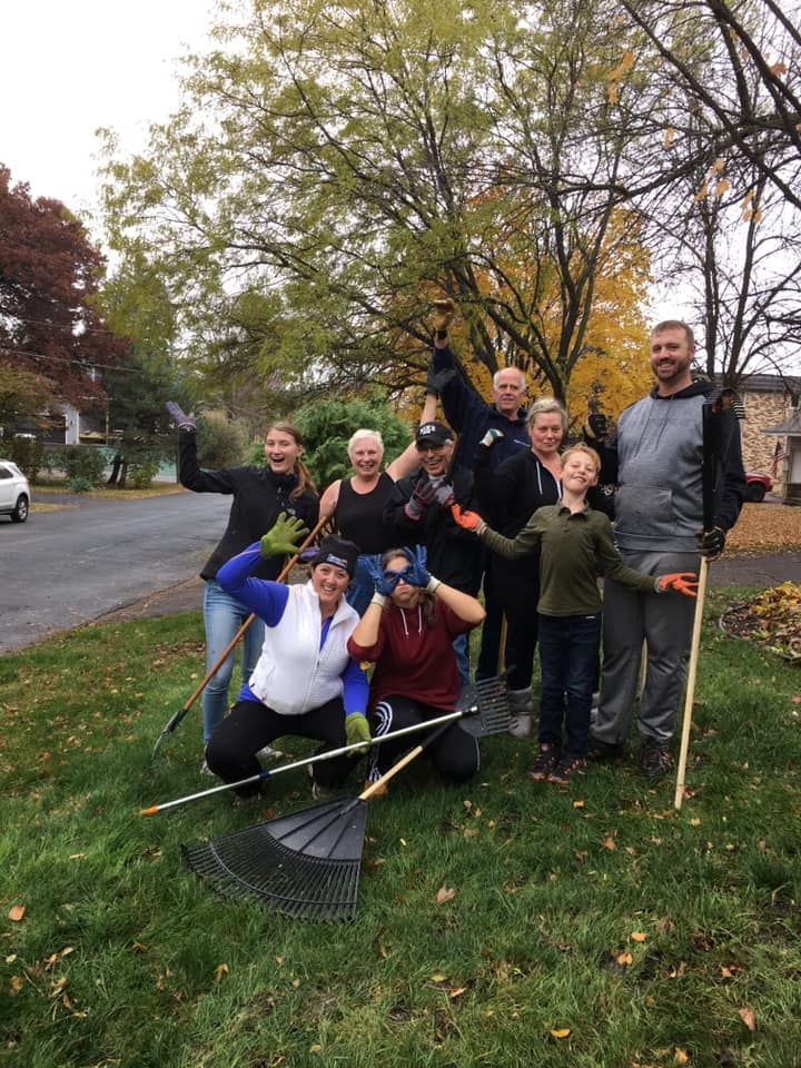 A group of people raking leaves, posing on a lawn, cloudy day.
