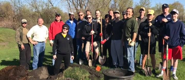 A group of people standing with shovels in a grassy area, some near a hole.