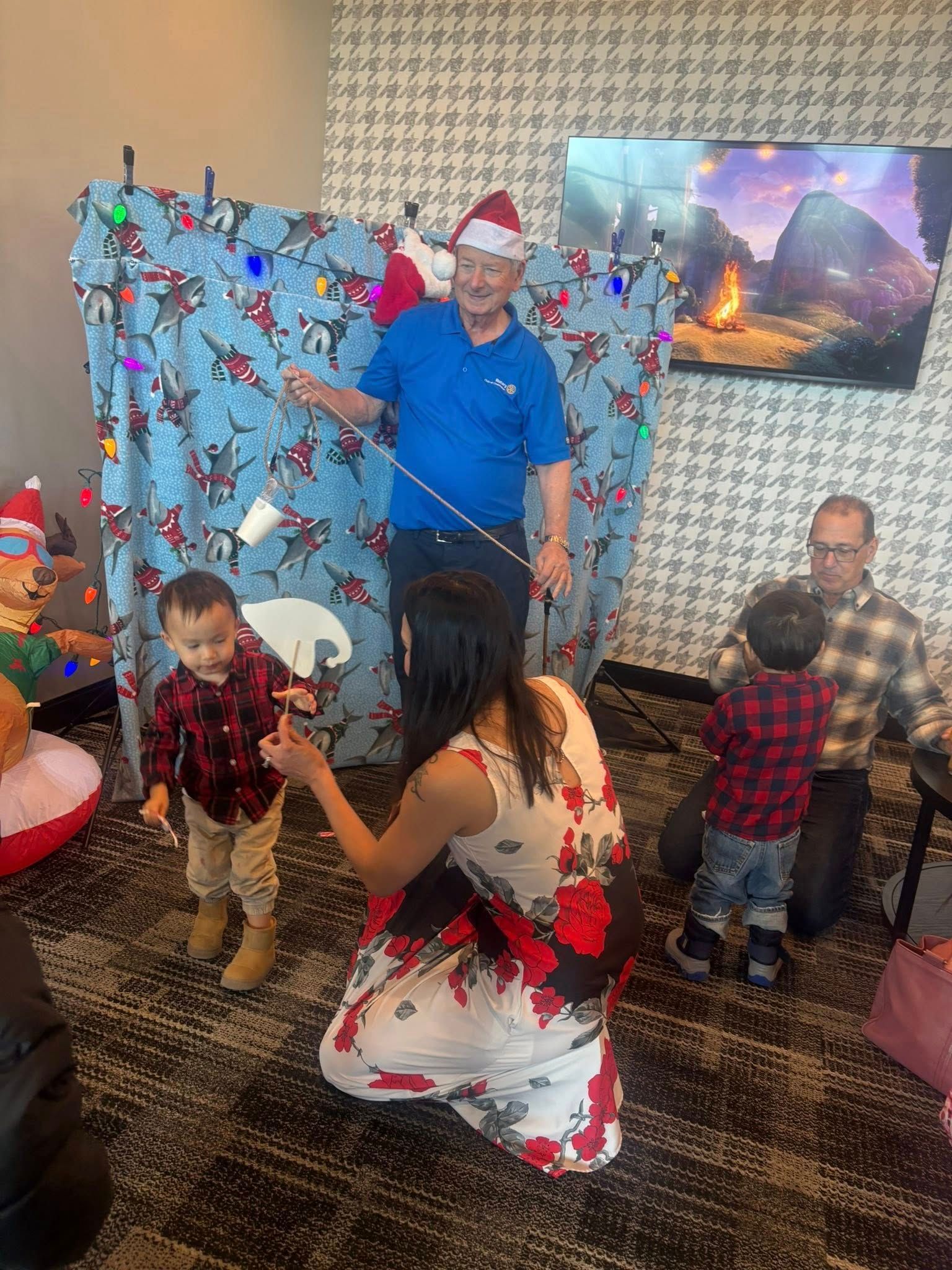 People playing a Christmas game in a room. A man in a Santa hat guides, and children try to catch items hanging on a backdrop.