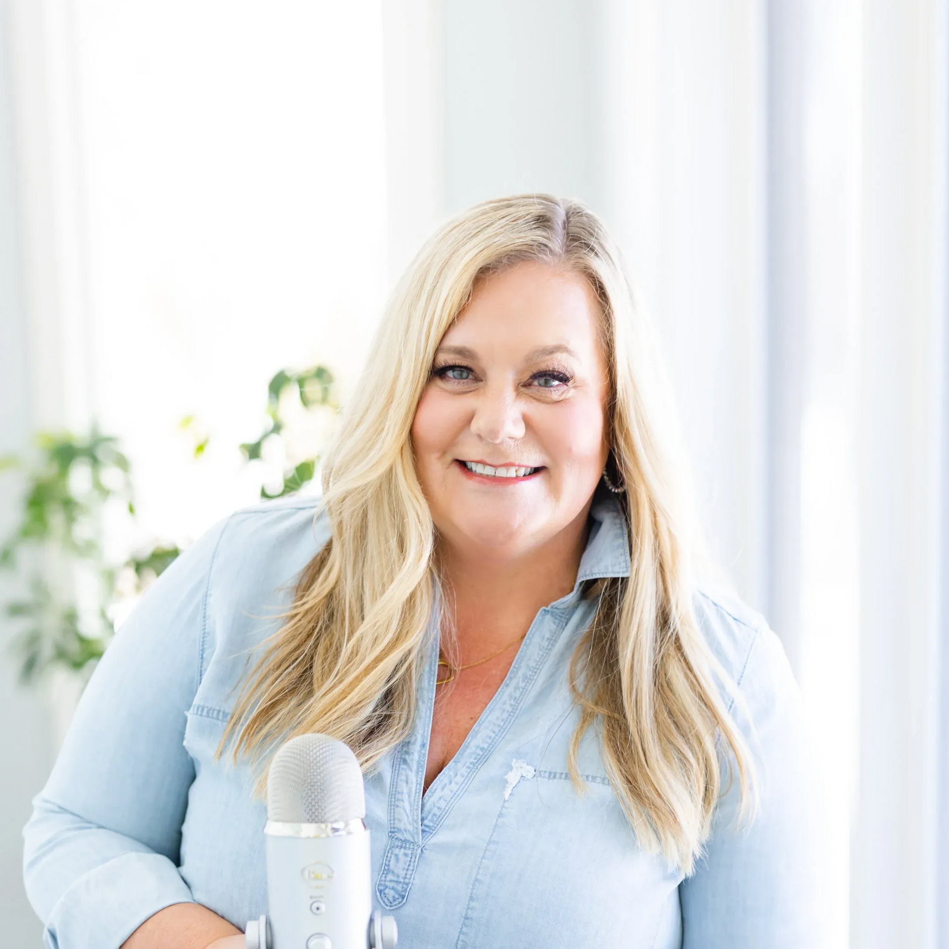 Two smiling women in business attire pose in front of a tan wall.