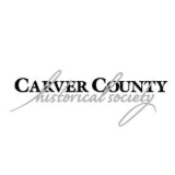 Two smiling women in business attire pose in front of a tan wall.