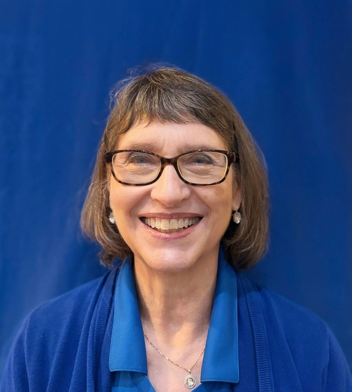Woman with glasses smiles in front of a blue background.