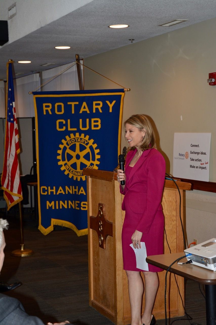 Woman in pink suit speaks at Rotary Club podium, Chanhassen, MN.