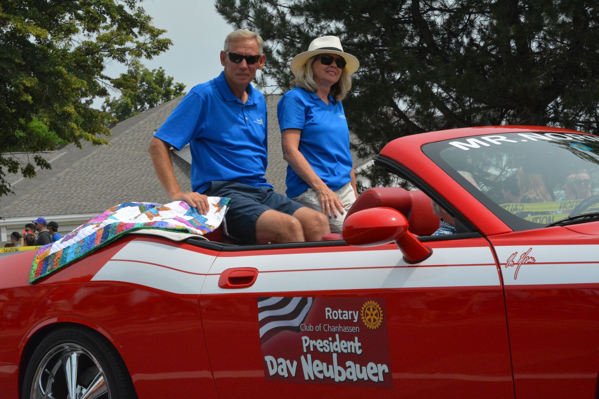 Man and woman in a red convertible. They wear blue shirts, riding in a parade.