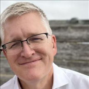Rotary Club meeting; people seated at tables, speaker at podium showing a slide, American flag in background.