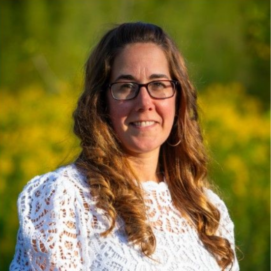 Rotary Club meeting; people seated at tables, speaker at podium showing a slide, American flag in background.