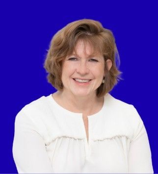 Woman with short brown hair smiles, wearing a white sweater, against a blue background.
