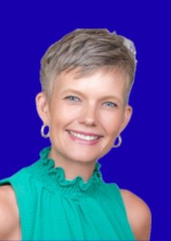 Woman with short blonde hair smiles, wearing a green top and silver hoop earrings, against a blue background.