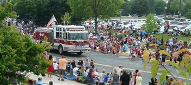Fire truck in a parade, lined with spectators on the side of the road with an American flag attached.