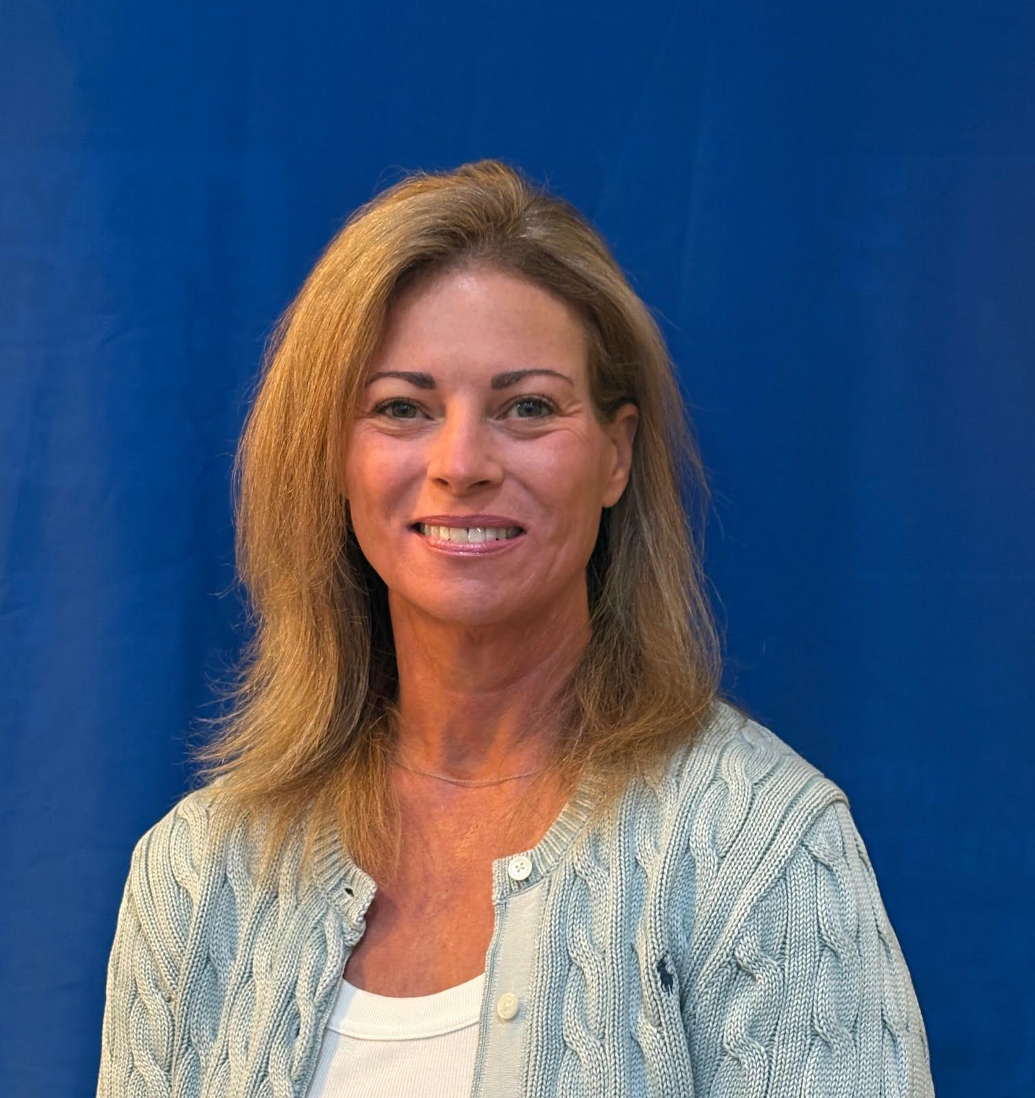 Woman with blonde hair wearing a light blue cardigan smiles against a blue backdrop.