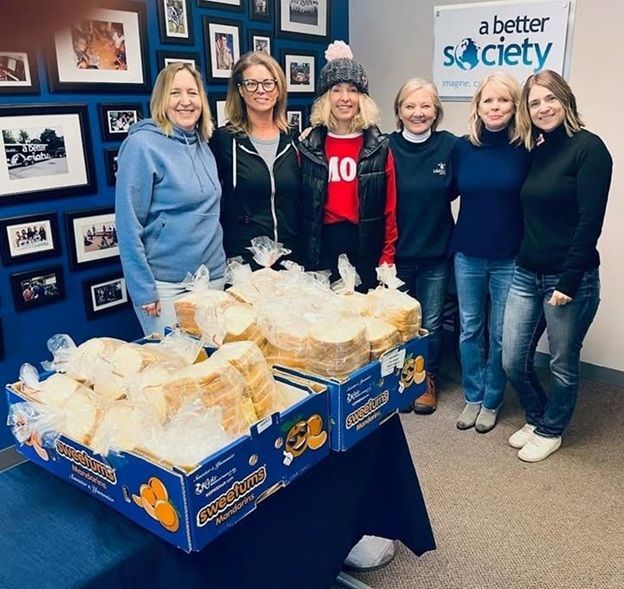 Group of people with bread, in front of a blue wall with framed pictures and a 
