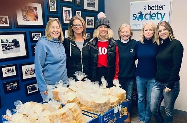 Six people stand with loaves of bread, near a